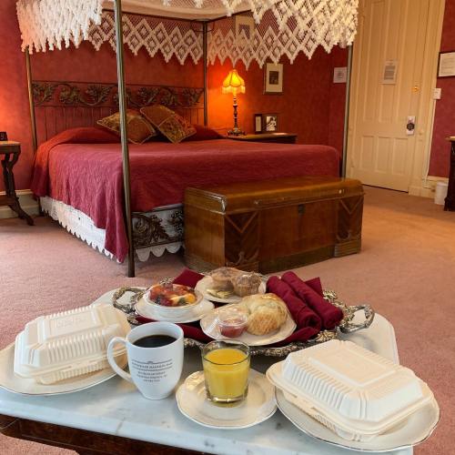 A cozy bedroom with a red bedspread, a breakfast tray featuring pastries, fruit, coffee, and juice in the foreground.