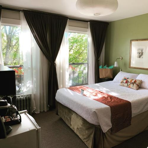 Cozy bedroom with a bed, green walls, large windows, and curtains, featuring a small desk and decorative items.
