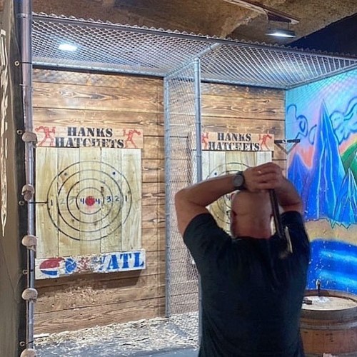 A person stands in an axe-throwing venue, preparing to throw an axe at a target on the wall.