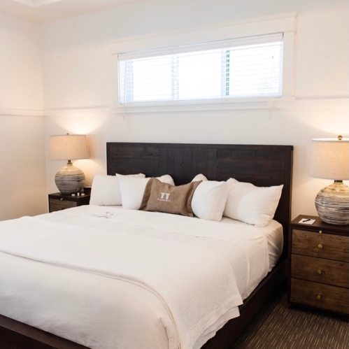 Cozy bedroom featuring a large bed with white linens, two bedside lamps, and a window with blinds.