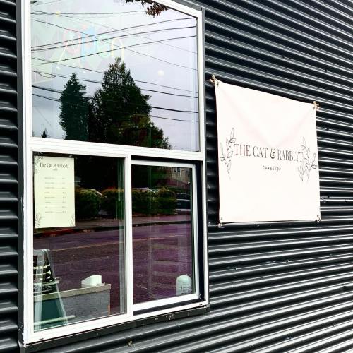 A window view of a café called "The Cat & Rabbit," featuring a menu and a sign on a textured wall.