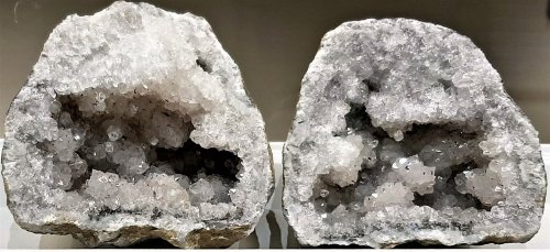 Two geodes split open, revealing clusters of sparkling gray and clear crystals inside.