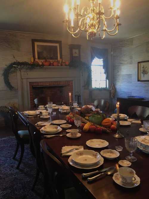 A beautifully set dining table with fine china, candles, and a centerpiece of fruits, in a warmly lit room.