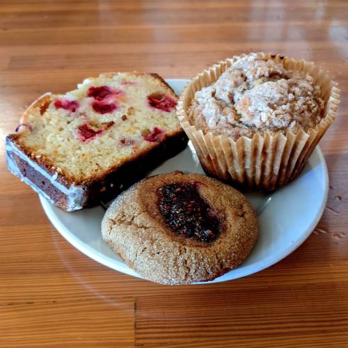 A plate with a slice of raspberry bread, a muffin, and a cookie, all on a wooden table.