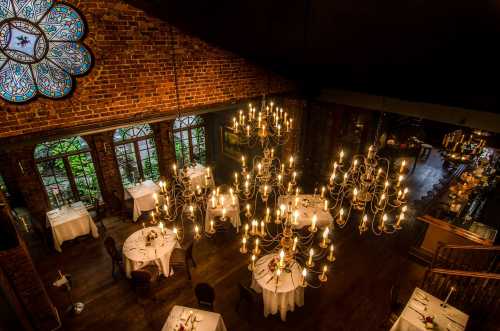 Elegant restaurant interior with chandeliers, round tables, and a stained glass window, creating a warm ambiance.