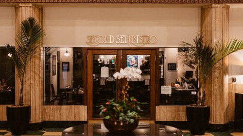 Entrance of Second Set Bistro, featuring large columns, potted plants, and a welcoming atmosphere.