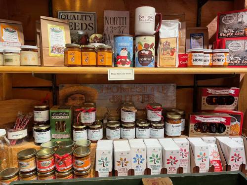A wooden shelf filled with various jars, honey, seeds, and packaged goods, showcasing local products and treats.