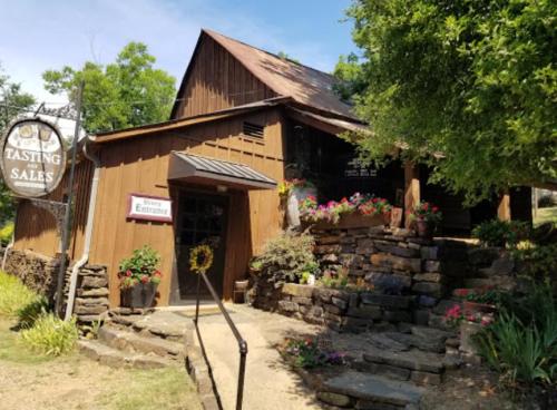 A rustic wooden building with a stone pathway, surrounded by colorful flowers and a sign for wine tasting sales.