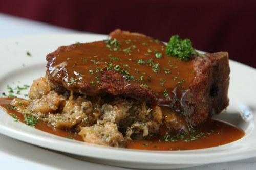 A plate of crispy meat topped with rich brown gravy and garnished with parsley, served over a bed of savory stuffing.