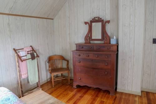 A cozy bedroom corner featuring a wooden dresser with a mirror, a chair, and a towel rack with colorful towels.