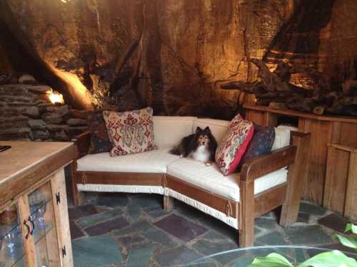 A cozy living space with a wooden couch, decorative pillows, and a small dog sitting on the couch in a rustic setting.