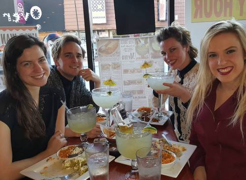 Four friends enjoying a meal with margaritas at a restaurant, smiling and having a good time together.