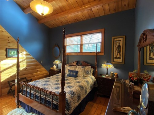 Cozy bedroom with a wooden ceiling, blue walls, a four-poster bed, and decorative lamps.