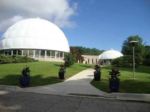 Two white dome-shaped buildings surrounded by green grass and plants, with a paved walkway leading between them.