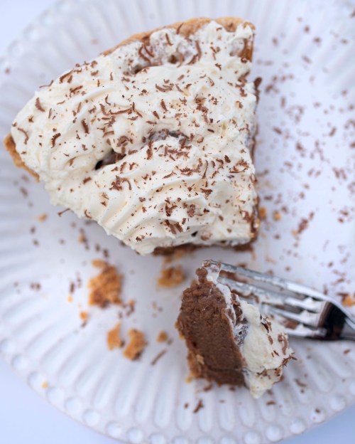 A slice of chocolate cream pie topped with whipped cream and chocolate shavings, with a fork resting beside it.