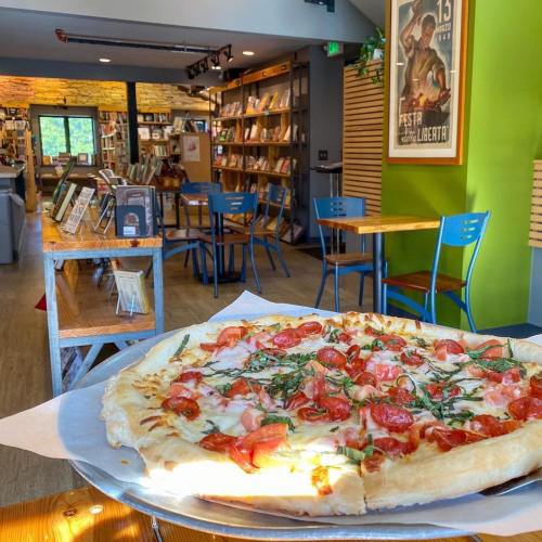 A delicious pizza topped with tomatoes and herbs, set in a cozy bookstore café with bookshelves in the background.