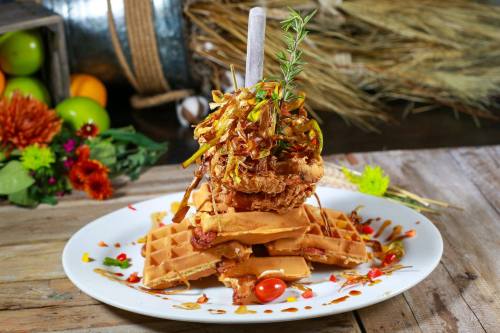 A stack of waffles topped with fried chicken, garnished with herbs and drizzled with sauce, served on a rustic plate.