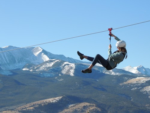 A person zip-lining against a backdrop of snow-capped mountains and a clear blue sky.