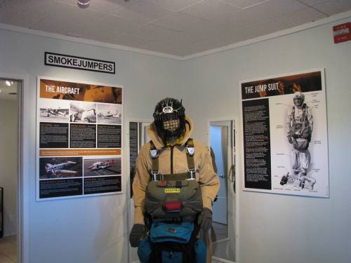 A display featuring a smokejumper mannequin, surrounded by informational posters about aircraft and jump suits.