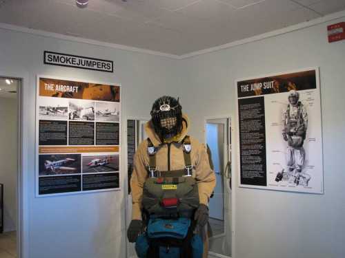 A display featuring a smokejumper mannequin, surrounded by informational posters about aircraft and jump suits.