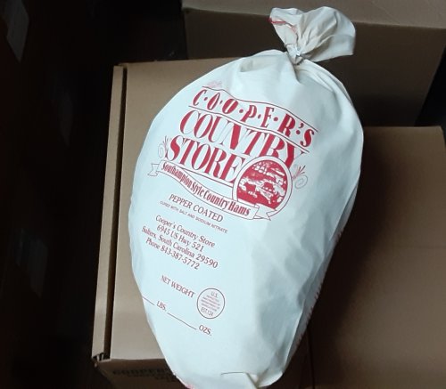 A large bag labeled "Cooper's Country Store" containing pepper-coated country hams, resting on cardboard boxes.