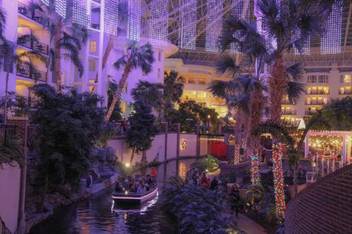 A vibrant indoor garden with palm trees, colorful lights, and a boat on a winding waterway.