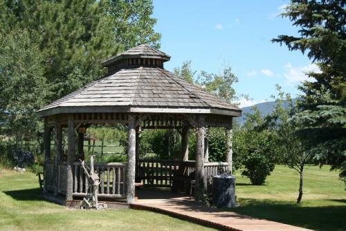 A wooden gazebo with a peaked roof surrounded by trees and grassy areas under a clear blue sky.