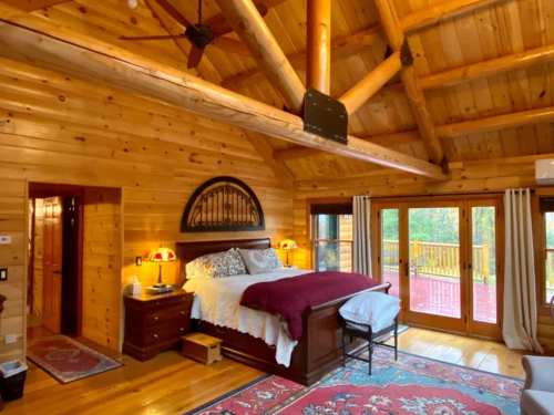Cozy wooden bedroom with a large bed, rustic decor, and sliding doors leading to a deck. Warm, inviting atmosphere.