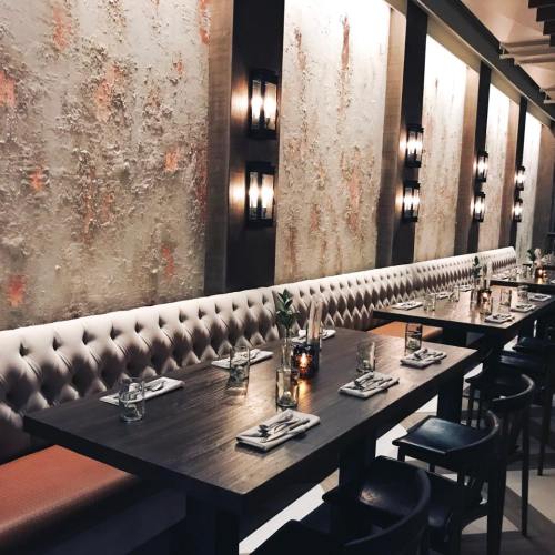 Elegant restaurant interior featuring tufted seating, wooden tables, and stylish wall sconces.