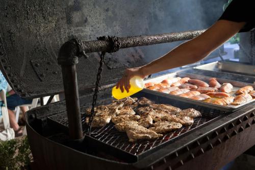 A person drizzles oil on grilled chicken and sausages on a large outdoor barbecue.