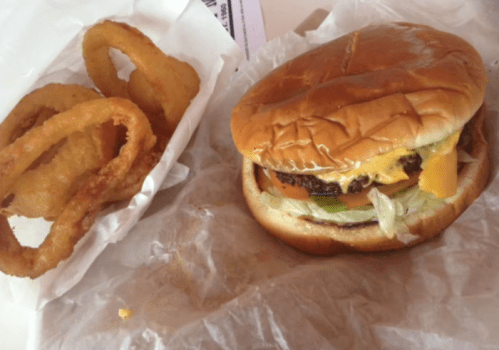 A cheeseburger with lettuce and tomato next to a serving of crispy onion rings on a white paper background.