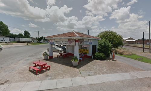 A small, colorful gas station with picnic tables outside, surrounded by greenery and a clear blue sky.