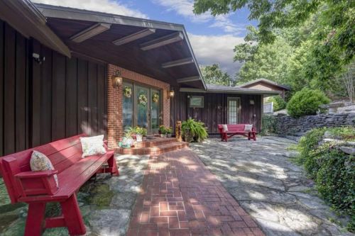 A cozy outdoor patio with red benches, stone pathways, and lush greenery surrounding a modern home.