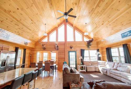 Cozy wooden living space with high ceilings, large windows, and a dining area, featuring rustic decor and comfortable seating.