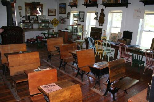 A vintage classroom with wooden desks, colorful chairs, and various educational artifacts displayed on the walls.