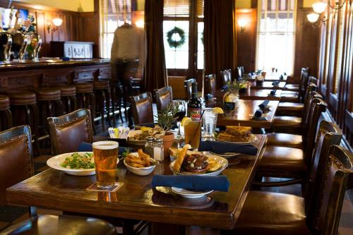 A cozy restaurant interior with wooden tables, chairs, and a bar, featuring plates of food and drinks on the tables.
