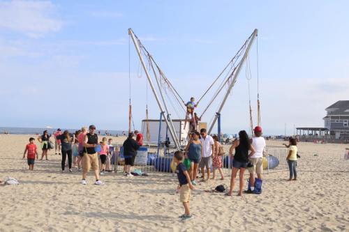 A busy beach scene with families enjoying a bungee trampoline attraction under a clear sky.