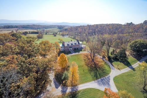 Aerial view of a large mansion surrounded by colorful autumn trees and winding paths in a rural landscape.