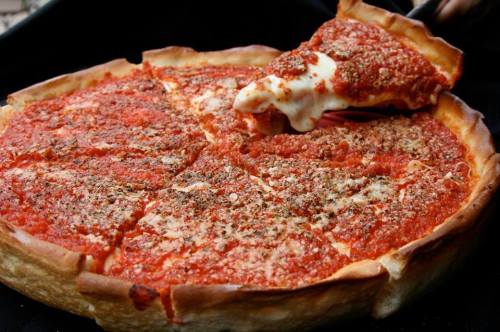 A deep-dish pizza with a thick crust, topped with tomato sauce and melted cheese, being served with a spatula.