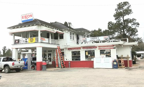 A two-story gas station and convenience store with a porch, featuring an Exxon sign and a red and white color scheme.