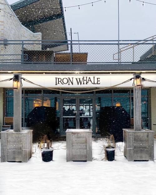 Exterior of Iron Whale restaurant in snowy weather, featuring wooden planters and a modern design.