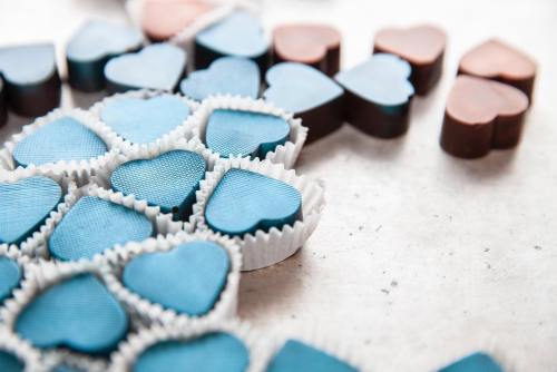 A close-up of heart-shaped chocolates in blue and brown, arranged on a light surface with paper liners.