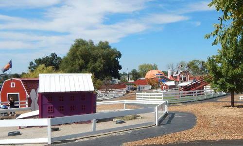 Colorful farm-themed playground with a purple barn, slides, and trees under a blue sky.