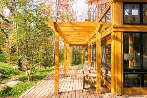 A wooden deck with chairs, surrounded by trees and colorful autumn foliage, next to a modern glass-walled cabin.