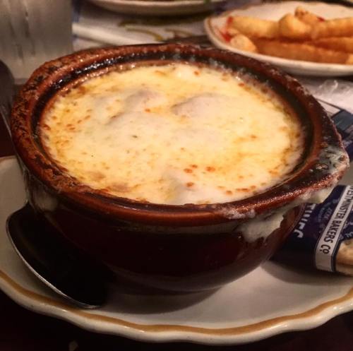 A bowl of French onion soup topped with melted cheese, served with a spoon on a table.