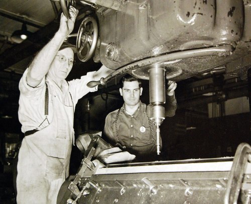 Two men operate a large industrial machine, focused on precision work in a workshop setting.