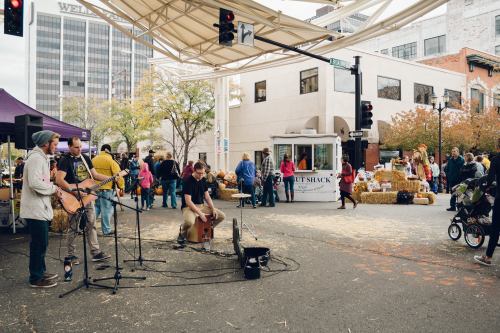 A lively street scene with musicians performing, food vendors, and a crowd enjoying a festival atmosphere.
