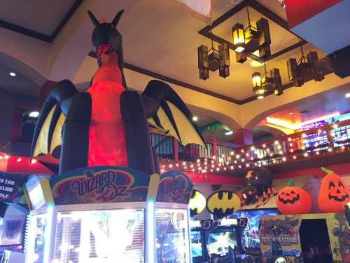 A large inflatable dragon towers over an arcade filled with colorful lights, games, and Halloween decorations.