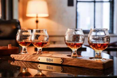 A wooden flight board with four glasses of whiskey, set in a cozy, well-lit room.