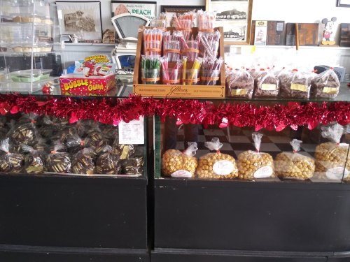 A display case filled with various candies and treats, including chocolate-covered items and popcorn, decorated with red garland.